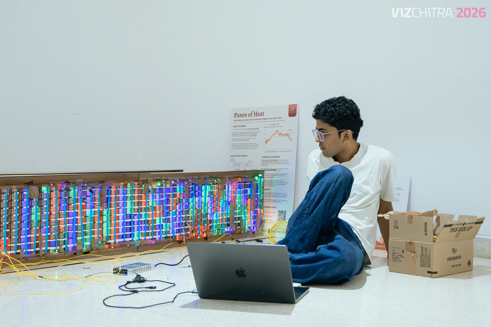 Team member seated on the floor beside the illuminated tower during setup, laptop connected to the installation